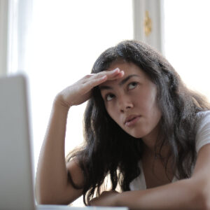 This image is a picture of woman with her hand on her forehead and a computer in front of her and she seems exhausted and overwhelmed.  Which is what it is like with the endless choices of making money online.